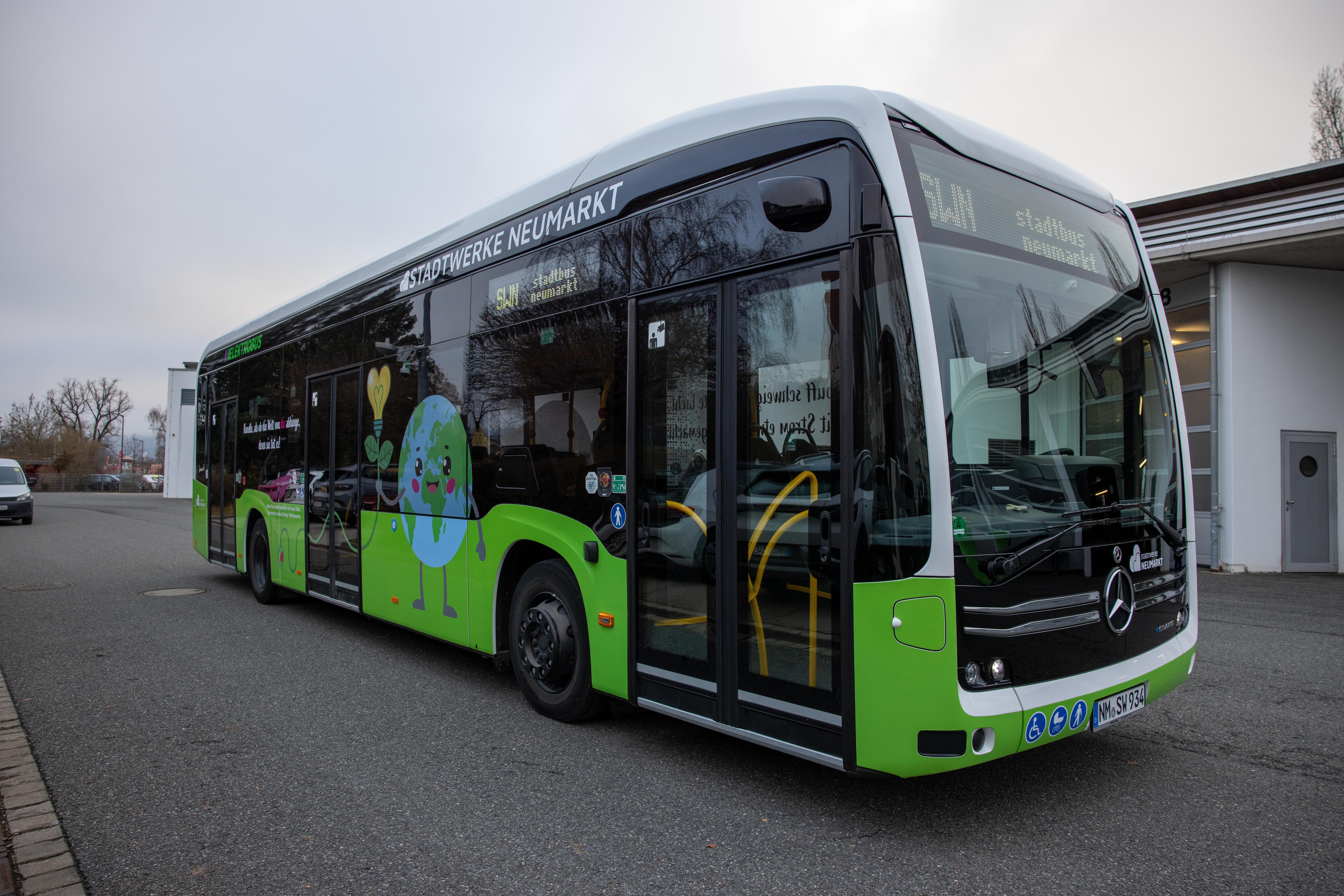 Ein grüner Stadtbus der Stadtwerke Neumarkt. Der Bus ist mit bunten Illustrationen zum Thema Umwelt und Nachhaltigkeit gestaltet, darunter eine lachende Erde und Pflanzen.