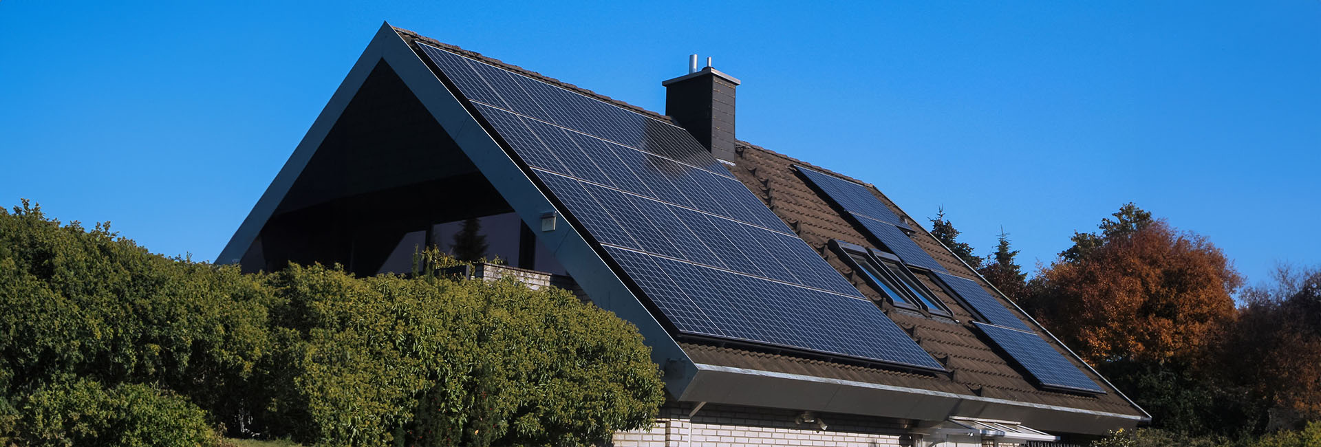 Wohnhaus mit Photovoltaikanlage auf dem Schrägdach bei strahlend blauem Himmel und Sonnenschein.