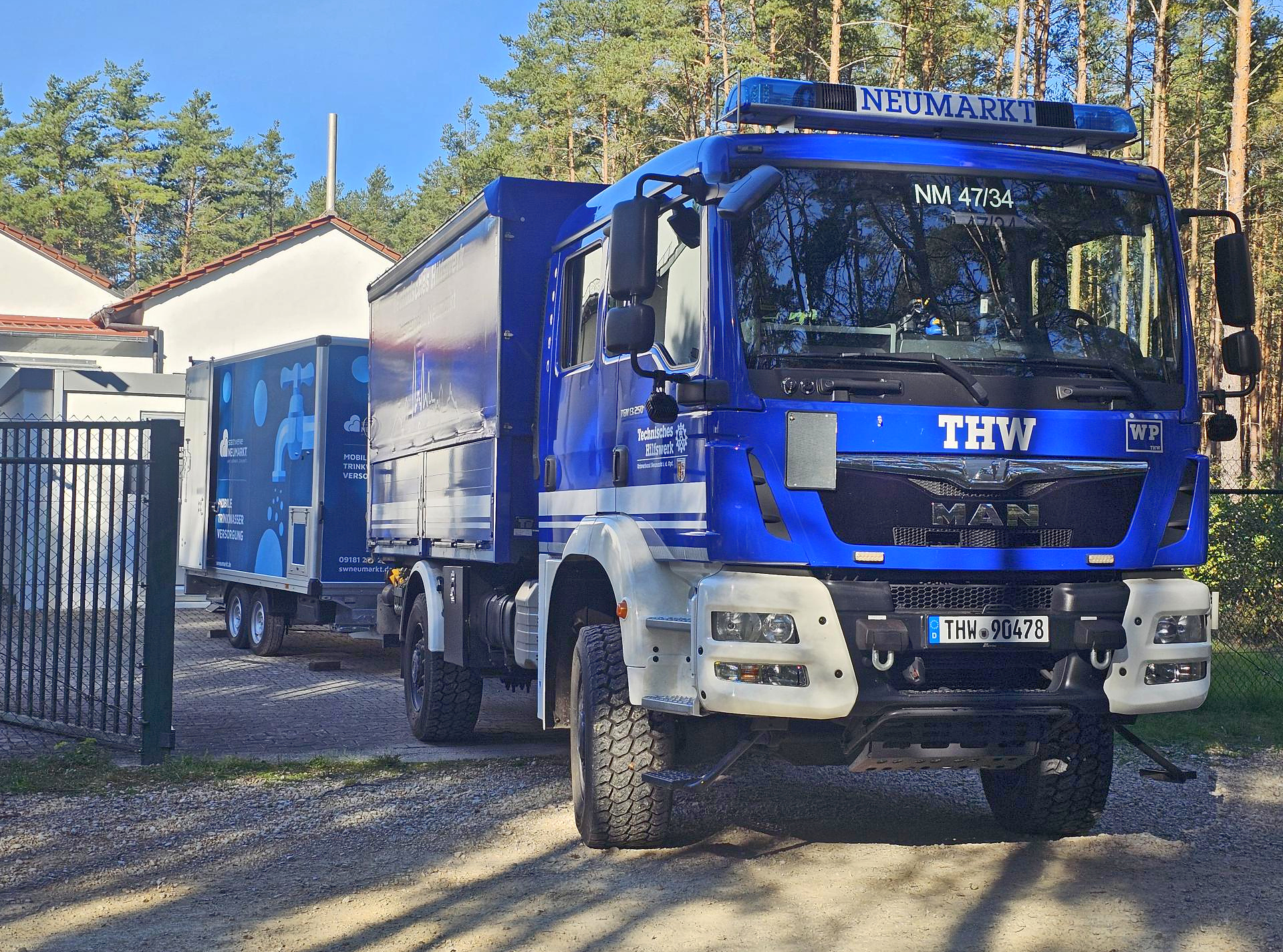 Blauer THW-Lkw mit angekoppeltem Notwasseranhänger der Stadtwerke Neumarkt auf einem Betriebsgelände.